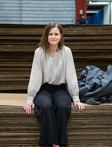 Johanna Ljunggren, Nachhaltigkeitsmanagerin bei Kinnarps, auf einem Stapel aus Kartonagen sitzend